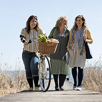Three Ladies walking along a path wih a bike with on earing a compression stocking